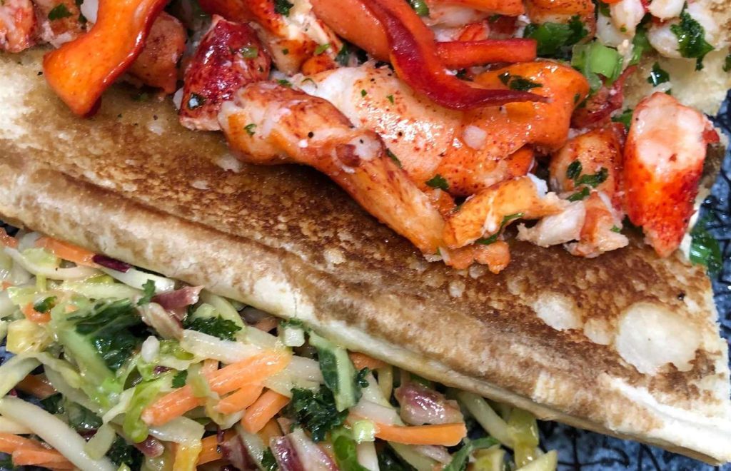 Connecticut Lobster Roll: Delicate lobster meat tossed in warm butter, lemon juice, scallions and parsley served on a toasted lobster roll with a side of super slaw